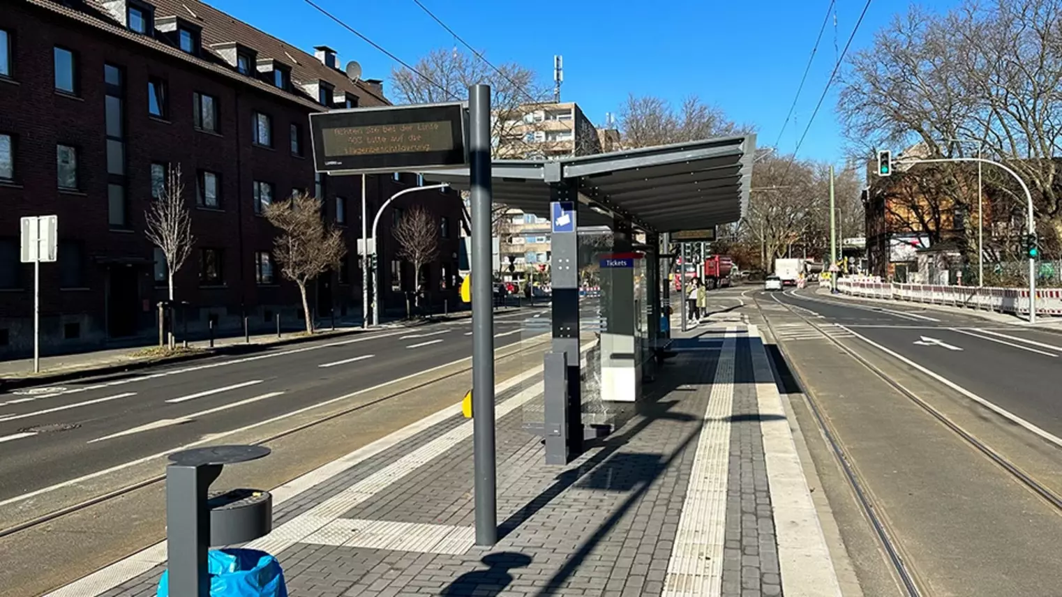 Neubau Haltestelle Brückelstraße: Blick auf die fertige Haltestelle mit Wetterschutz, dynamischen Fahrgastinformation, Mülleimer, Ticketautomat und Sitzgelegenheiten, im Hintergrund ist ein Fahrgast zu sehen